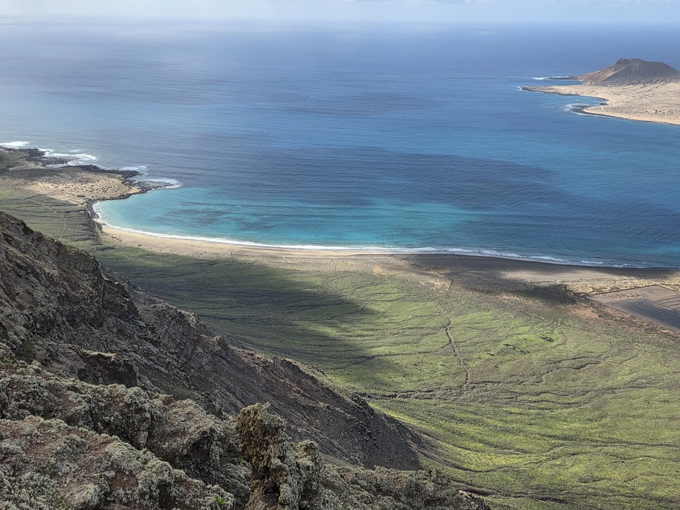 A turquoise cove and volcanic island from a high cliff